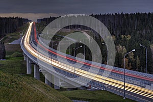 Light trails on four lane highway, crosses the night forest.