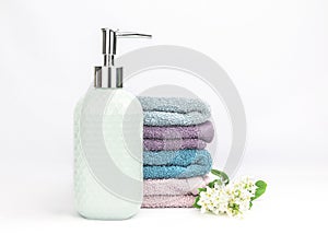 Light turquoise ceramic soap dispenser with multicolored soft towels and fresh flowers on a white background