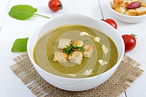 Light vegan spinach cream soup with crispy croutons in a bowl on a white background