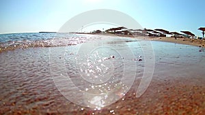 Light waves surf surf on the sandy beach with thatched beach umbrellas on a clear sunny day, Red Sea, view from below, wide angle.