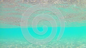 Light waves surf surf on the sandy beach with thatched beach umbrellas on a clear sunny day, Red Sea, view from below, wide angle.