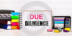 On a light wooden background, a calculator, multi-colored sticks and a notebook with the text DUE DILIGENCE. Business concept