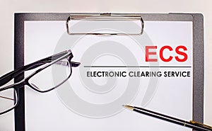 On a light wooden background glasses, a pen and a sheet of paper with the text ECS Electronic Clearing Service. Business concept