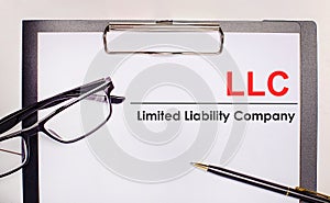 On a light wooden background glasses, a pen and a sheet of paper with the text LLC Limited Liability Company. Business concept