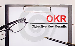 On a light wooden background glasses, a pen and a sheet of paper with the text OKR Objective Key Results. Business concept