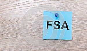 On a light wooden background - a light blue square sticker with the text FSA Flexible Spending Account