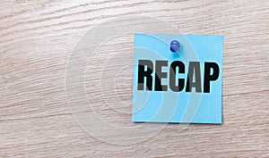 On a light wooden background - a light blue square sticker with the text RECAP