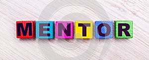 On a light wooden background, multi-colored wooden cubes with the text MENTOR