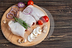 On a light wooden board, fresh skinless chicken thighs, next to mushrooms, with tomatoes, red onions and rosemary. Recipe of dish