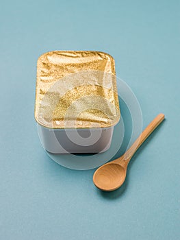 Light wooden spoon with a closed food container on a blue background.