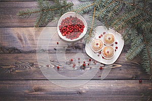A light wooden table top with a plate of freshly baked muffins decorated with red berries sprinkled with white powder and a plate
