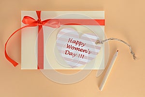 Light yellow envelope with a red ribbon and heart Happy Women Day card on an apricot background