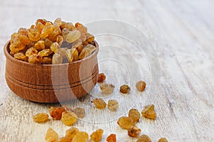 Light yellow raisins in a wooden bowl on a light white background. Close-up. Isolated