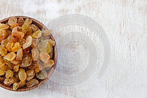 Light yellow raisins in a wooden bowl on a light white background. Close-up. Isolated