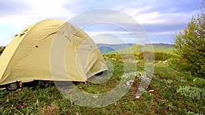 Light yellow tent sways in strong wind at beautiful morning mountain landscape