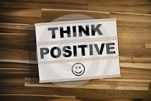 Lightbox or light box with happy smiley and message Think positive on a wooden table