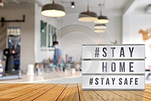 Lightbox sign with text hashtag  STAY HOME and  STAY SAFE with blurred barista, blurred coffee shop background. COVID-19. Stay