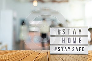 Lightbox sign with text hashtag #STAY HOME and #STAY SAFE with blurred customer, blurred coffee shop background. COVID-19. Stay