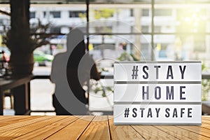 Lightbox sign with text hashtag  STAY HOME and  STAY SAFE with woman shadow, blurred coffee shop background. COVID-19. Stay home