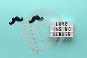 Lightbox with slogan LOVE HAS NO GENDER, paper props mustache on pastel cyan background