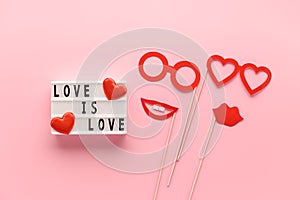 Lightbox with slogan LOVE HAS NO GENDER, red paper props glasses and lips on pastel pink background