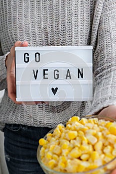 Lightbox with text GO VEGAN in female hands. Veganism, vegetarian healthy lifestyle. Frozen food in bowl. Yellow corn