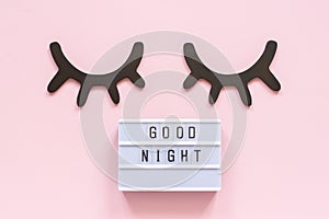 Lightbox text Good Night and decorative wooden black eyelashes, closed eyes on pink paper background. Concept Sweet