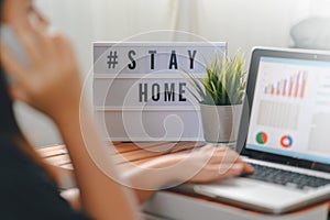 Lightbox with text hashtag  STAYHOME glowing in lightand blurred woman working at home. Office worker on quarantine. Home working photo