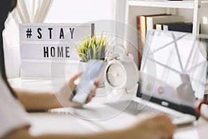 Lightbox with text hashtag #STAYHOME glowing in lightand blurred woman working at home. Office worker on quarantine. Home working
