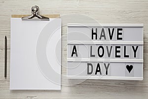 Lightbox with text `Have a lovely day`, pencil and noticepad over white wooden background, top view. From above, flat lay,