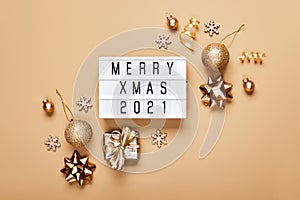 Lightbox with text MERRY XMAS 2021 and golden christmas decor on beige background. Creative layout in neutral monochrome colors