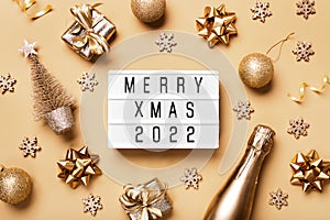 Lightbox with text MERRY XMAS 2022 and golden christmas decor on beige background. Creative layout in neutral monochrome