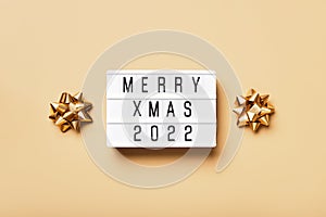 Lightbox with text MERRY XMAS 2022 and golden christmas decor on beige background. Creative layout in neutral monochrome