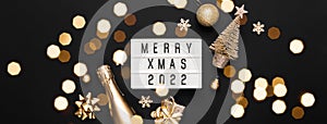 Lightbox with text MERRY XMAS 2022 and golden christmas decor on black background. Creative layout in monochrome colors