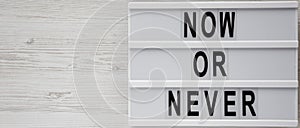 Lightbox with text `Now or never` word on modern board on a white wooden background, top view. Copy space