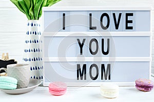 Lightbox with title Ilove you mom and tender tulips, macaroons on white wooden background. Mothers day decoration concept. photo