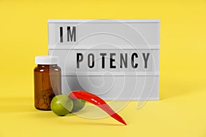 Lightbox with word IMPOTENCY, jar of pills and products symbolizing male sexual organ on yellow background photo
