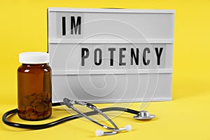 Lightbox with word IMPOTENCY  jar of pills and stethoscope on yellow background photo