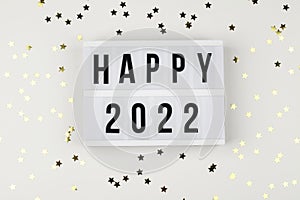 lightbox with words happy 2022 and holiday confetti on white background. top view new year celebration.