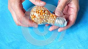 Lightbulb filled with popcorn seeds in hands