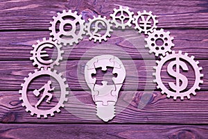 Lightbulb, gear, office worker, currency on a wooden background.