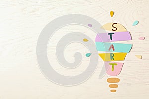 Lightbulb with word Start made of paper sheets on white wooden background, flat lay. Space for text