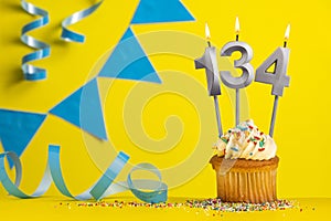 Lighted birthday candle number 134 - Yellow background with blue pennants