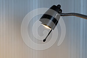 A lighted black reading lamp in front of white background with copy-space photo