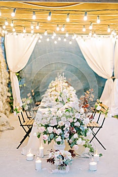 Lighted candles and a huge bouquet of flowers in a vase stand at the festive table on the terrace