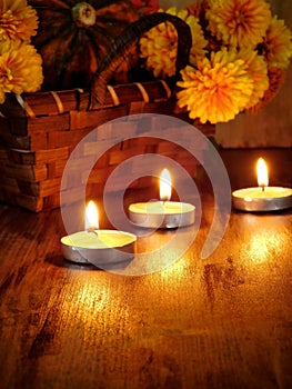 Lighted candles and a wicker basket with a pumpkin and flowers in the background