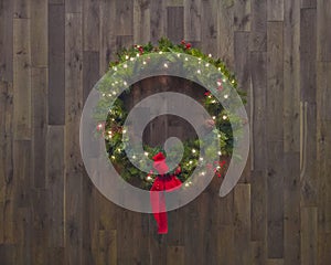 Lighted Christmas wreath, on wood background with red ribbon