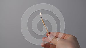 A lighted match burns with smoke on a gray background. Concept of slow-motion video with fire. The hand lights a match.