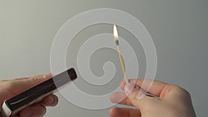 A lighted match burns with smoke on a grey background. Concept of slow-motion video with fire. The hand lights a match.