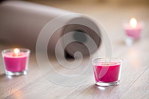 Lighted pink candle and rolled brown yoga, pilates mat on the fl photo